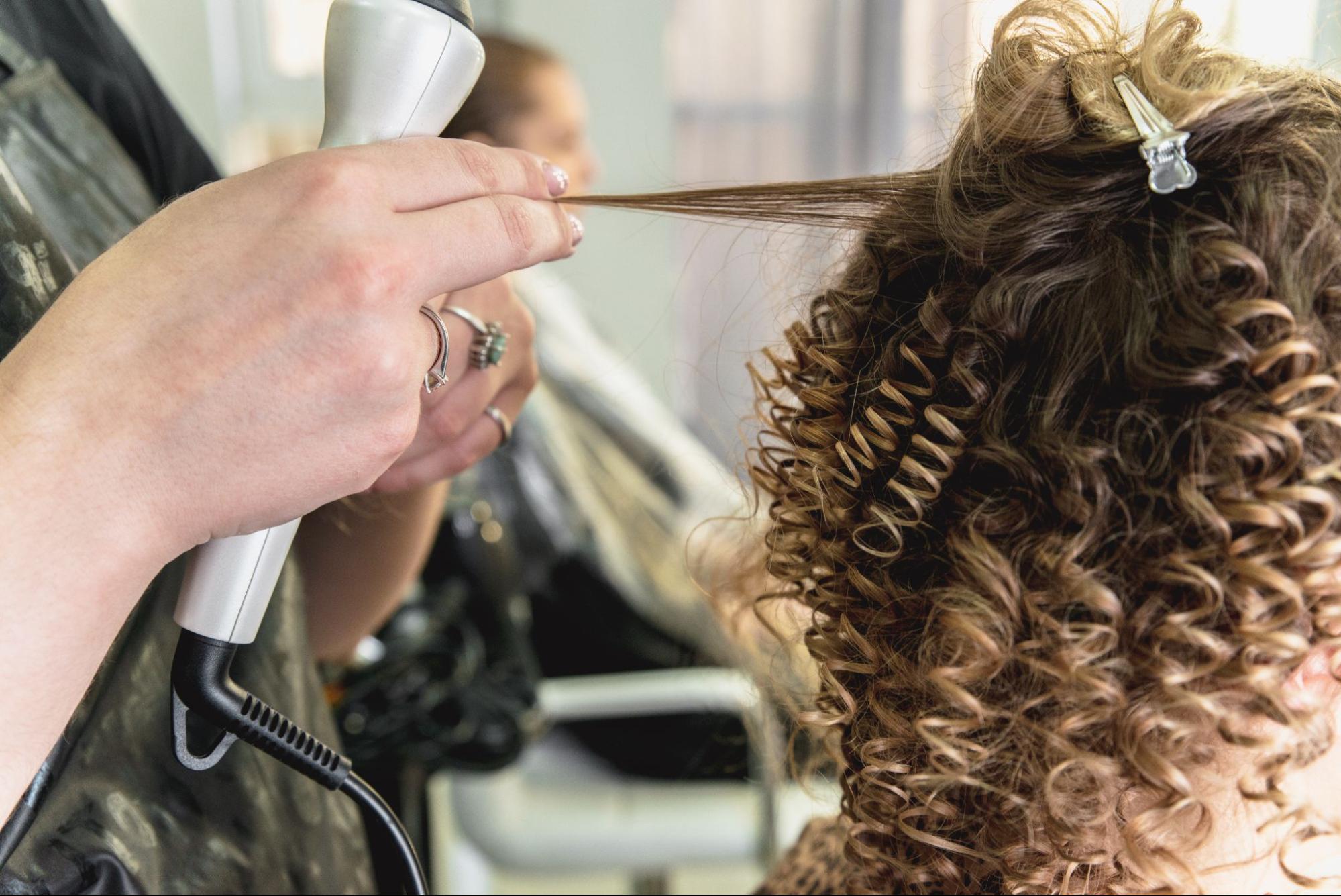 Zbliżenie na pracę stylisty podczas zabiegu trwałej ondulacji dla stylizacji włosów.